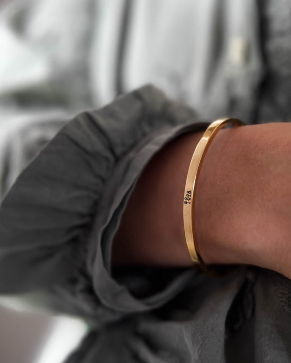 VENUS STICK bracelet in gold-plated stainless steel with engraved matchstick family, worn on the wrist with a grey blouse