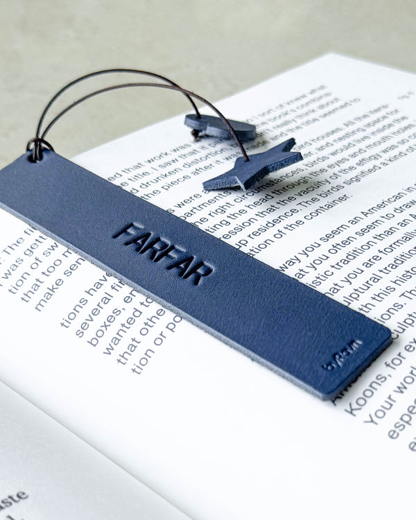 PAGE bookmark in navy blue leather with the engraving "Farfar" lying on an open book with star and heart on a cord