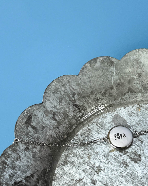 IBI STICK bracelet in silver-coloured stainless steel with an engraved matchstick family of three, on a zinc tray against a blue background