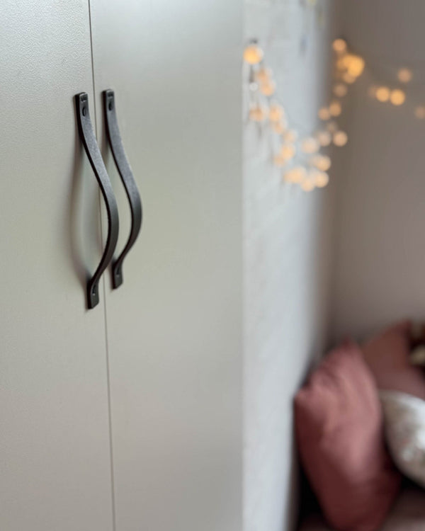 BAND leather handles in dark brown on a light wardrobe with two doors, fairy lights and pink cushions in the background
