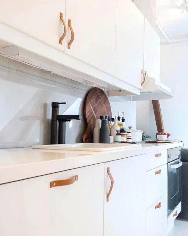 BAND leather drawer pulls in cognac fitted on white kitchen doors and drawers in a bright kitchen with black tap