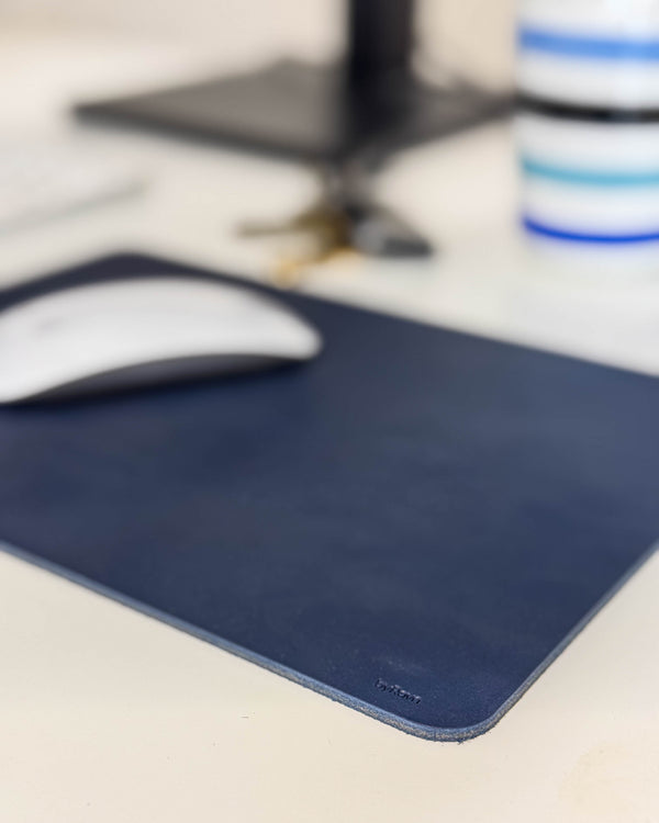DOS mouse pad in navy blue leather with a white mouse on a desk by a monitor stand and striped cup