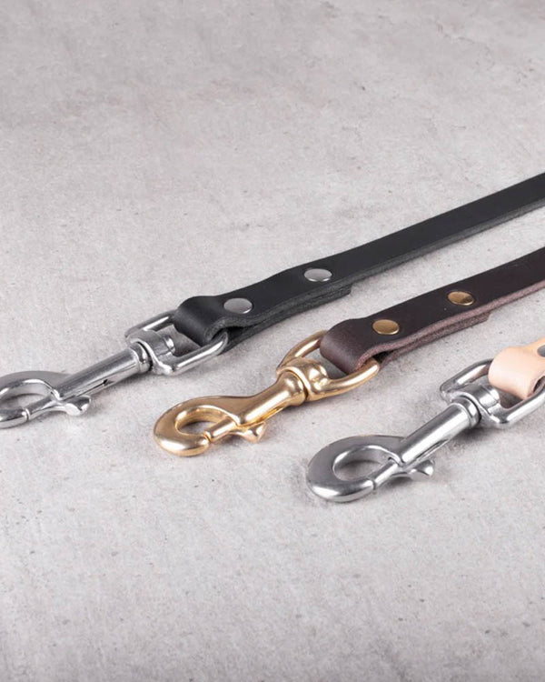 DOX160 leather dog leash in black leather with stainless steel carabiner, shown with dark brown and natural leash on concrete floor