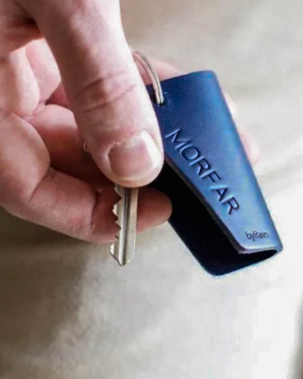 FOLD leather key holder in navy blue with personalised engraving "Morfar", held in hand with the key folded out