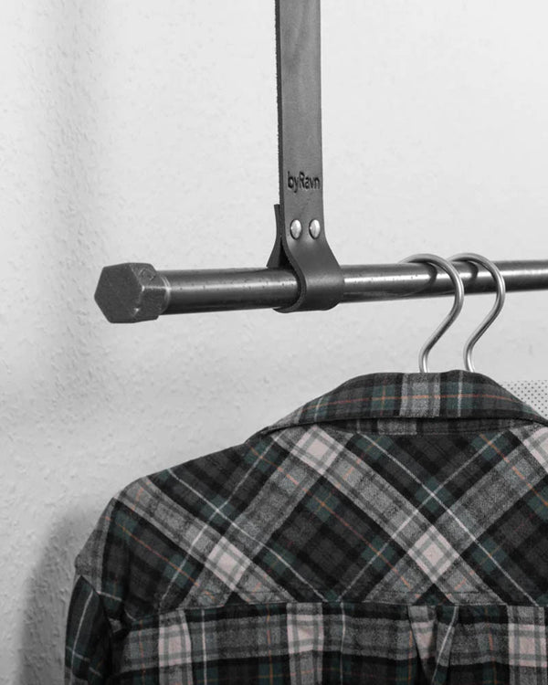 HOLD 30 hanging strap in black leather with two rivets and byRavn embossing around a metal rail with a checked shirt on a hanger