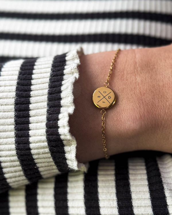 IBI X bracelet in gold-plated stainless steel with cross, letters and heart engraved, worn on the wrist with a striped blouse