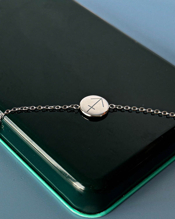 IBI STAR bracelet in silver-coloured stainless steel with the zodiac sign Sagittarius engraved on a round disc, lying on a dark green box