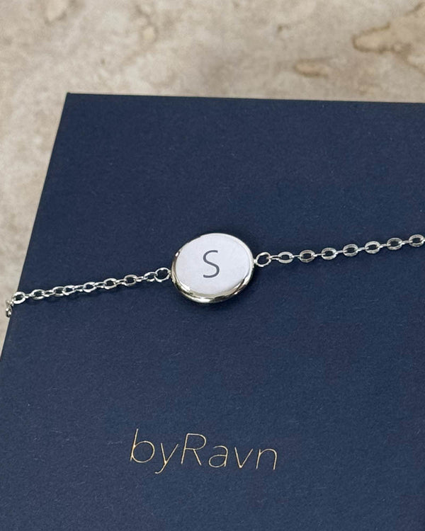 IBI LETTER bracelet in silver-coloured stainless steel with the letter "S" engraved, lying on a navy blue byRavn jewellery box
