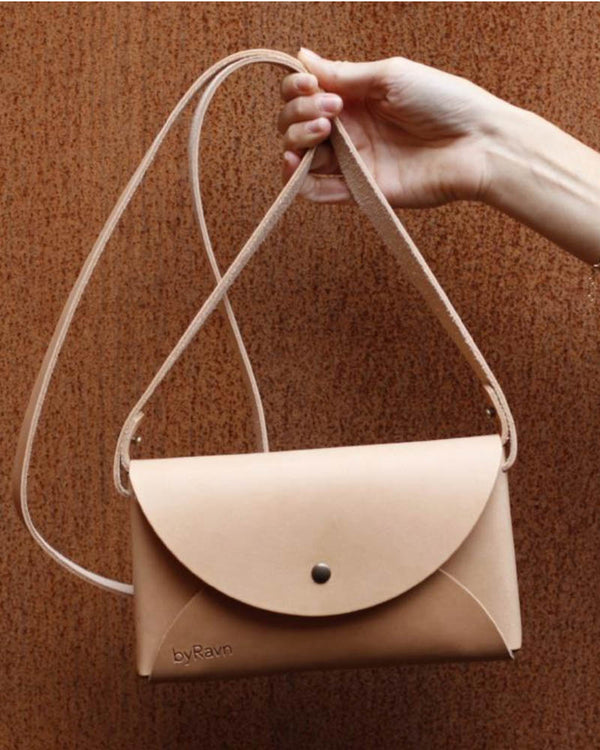 INA shoulder bag in natural leather held up by the strap against a rust-red wall