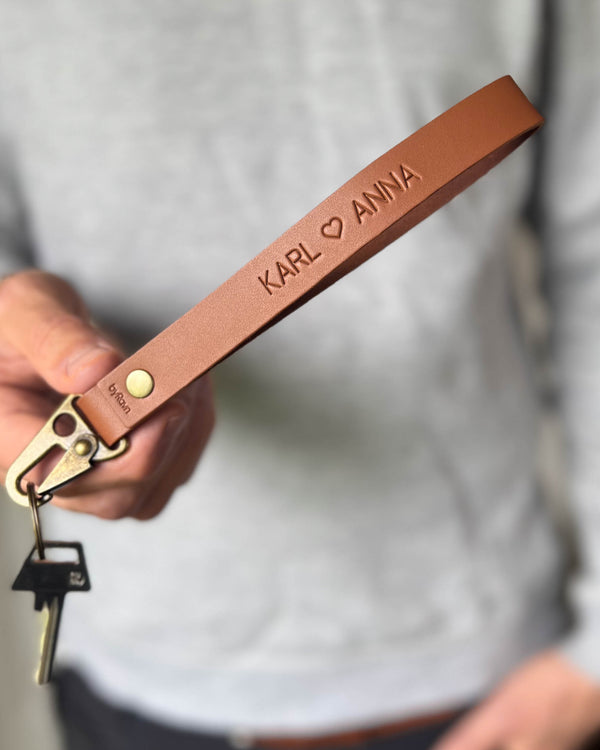 IRON leather keyring in cognac with the names "Karl ♡ Anna" engraved, held in hand with key