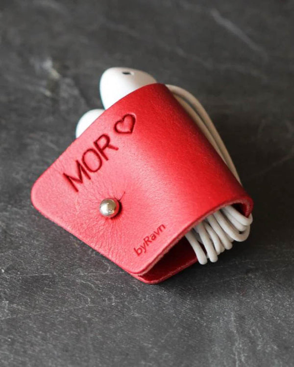 KAX earbud clip in red leather with the engraving "Mor" ♡ and white earbuds wrapped around, on dark slate