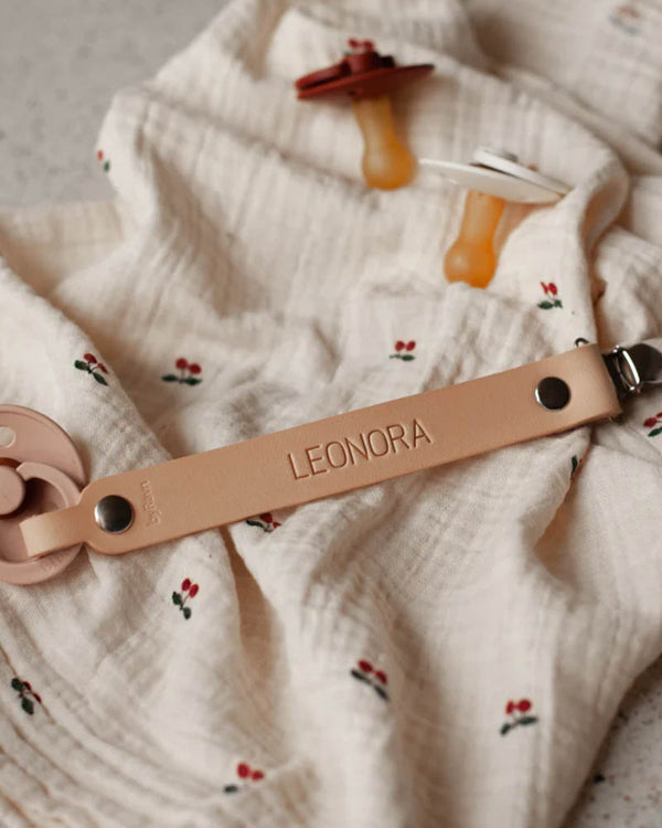 KODA dummy clip in natural leather with the name "Leonora" engraved, laid on a cherry-print muslin cloth with two dummies