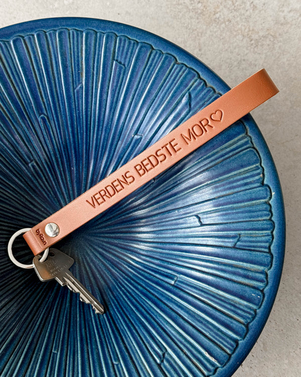 LUX leather keyring in cognac with the engraving "Verdens bedste mor" ♡ and key on a blue ribbed ceramic bowl