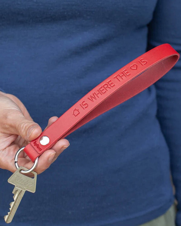LUX leather keyring in red with the engraving "Home is where the heart is" written with house and heart symbols, held in hand