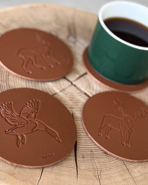 MOKKA hunting coasters in cognac leather embossed with flying mallard, roebuck and red deer stag on a wooden slab with green coffee cup