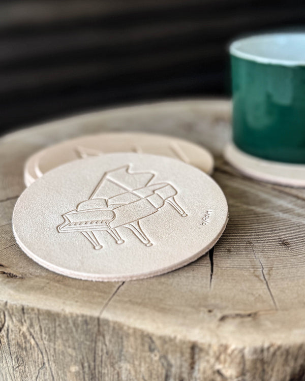 MOKKA music coaster in natural full-grain leather embossed with a grand piano on a tree stump by a green cup
