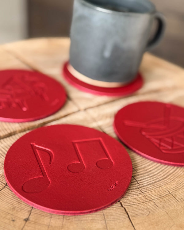 MOKKA music coasters in red leather embossed with sheet music, grand piano and drum on a wooden table with a grey ceramic cup
