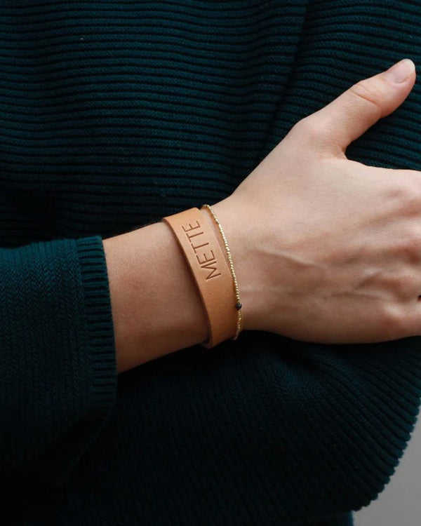 MONO leather bracelet in natural with the name "Mette" engraved on the wrist alongside a thin gold-coloured bracelet