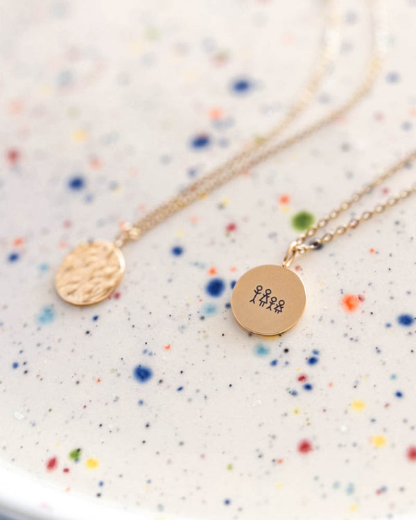 MOON STICK necklace in gold-plated stainless steel engraved with matchstick family of four, hammered coin alongside, on dotted ceramic dish