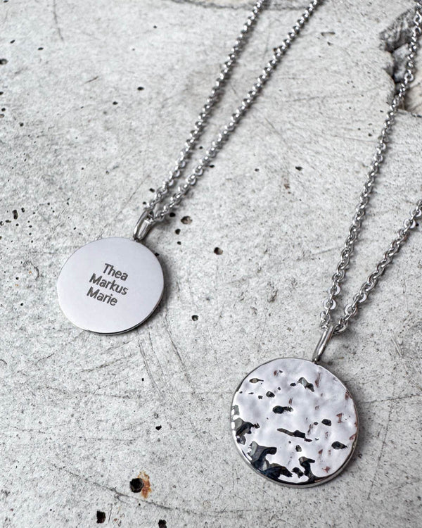 MOON QUOTE name necklace in silver-coloured stainless steel engraved with names "Thea Markus Marie", hammered side alongside, on concrete