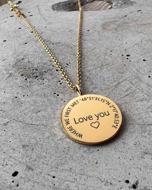 SIA CIRCLE necklace in gold-plated steel with "Love you" ♡ and "Where we first met" with coordinates engraved in a circle, on concrete