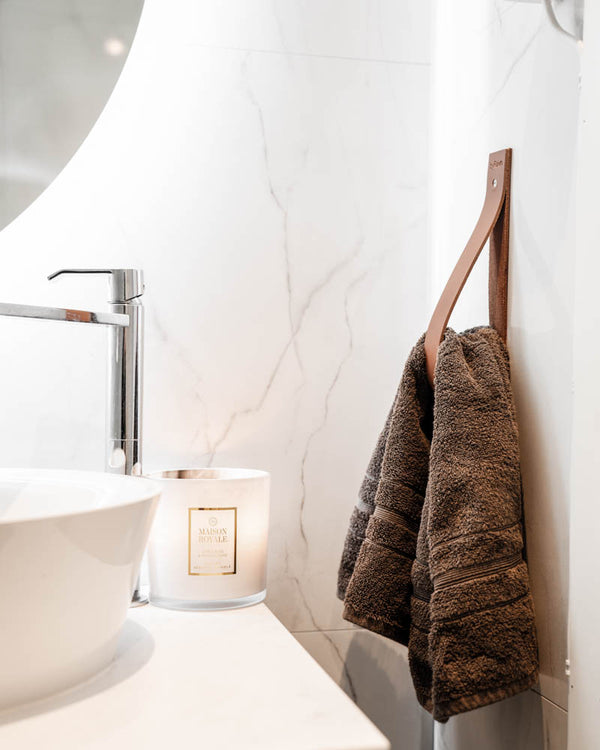 STACK magazine holder in cognac leather used as a towel holder in a bathroom with marble wall and scented candle