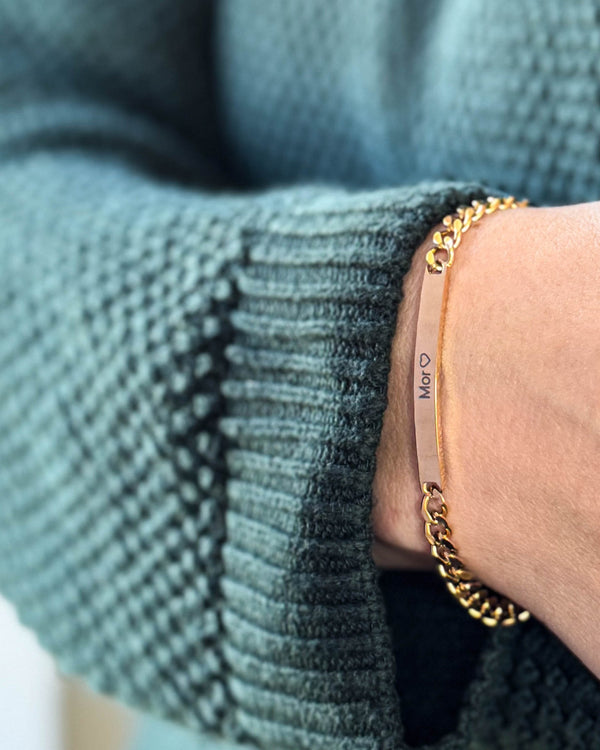 ZOE bracelet in gold-plated stainless steel with the engraving "Mor" ♡ on a bar plate, worn on the wrist with a green knit