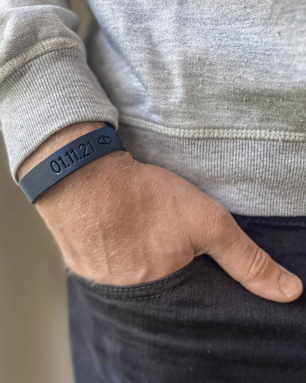 MONO leather bracelet in navy blue with the date "01.11.21" and a small symbol engraved on the wrist, hand in pocket