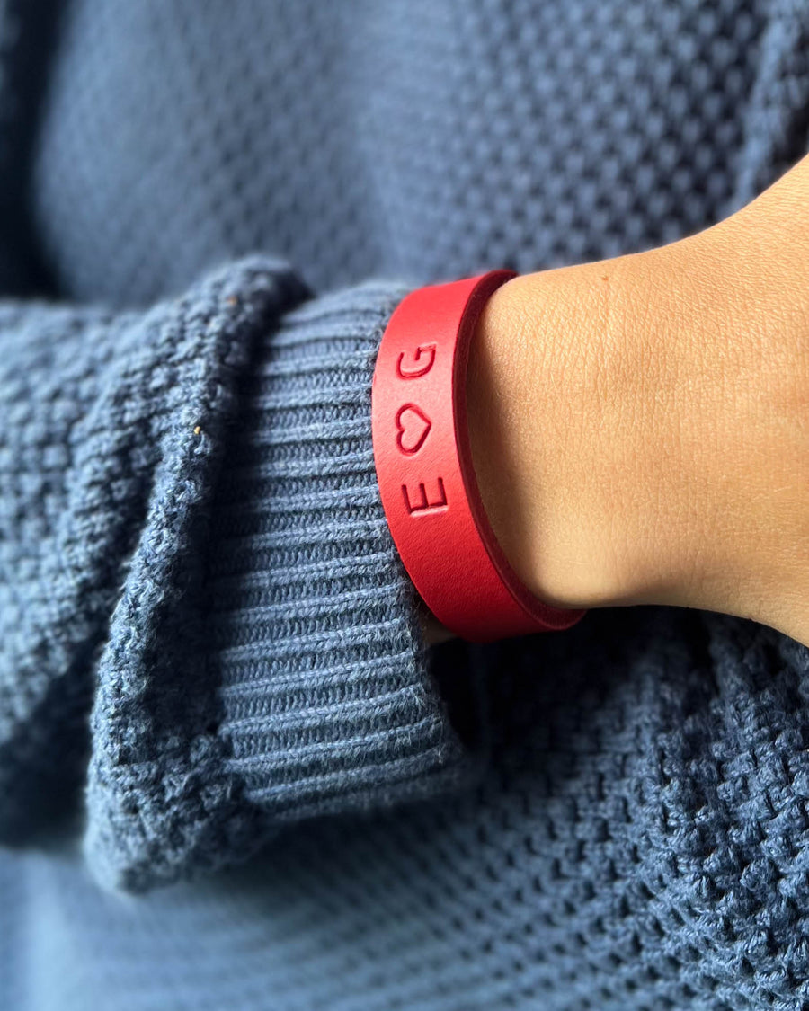 MONO leather bracelet in red with the initials "E ♡ G" engraved on the wrist, worn with a blue knit