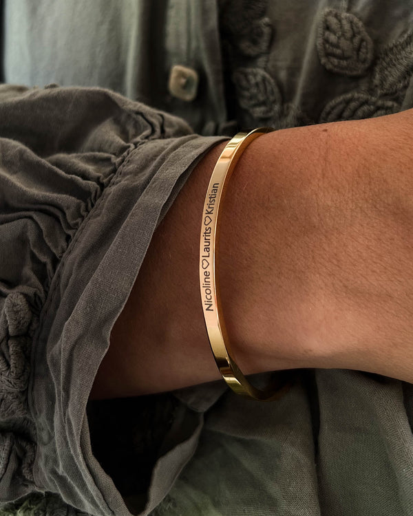 VENUS bracelet in gold-plated stainless steel with the engraving "Nicoline ♡ Laurits ♡ Kristian" on the wrist, grey blouse