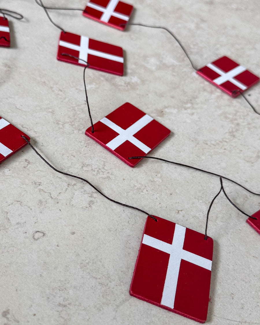 SALUT bunting with Dannebrog flags in red leather on black cord laid on a light stone surface