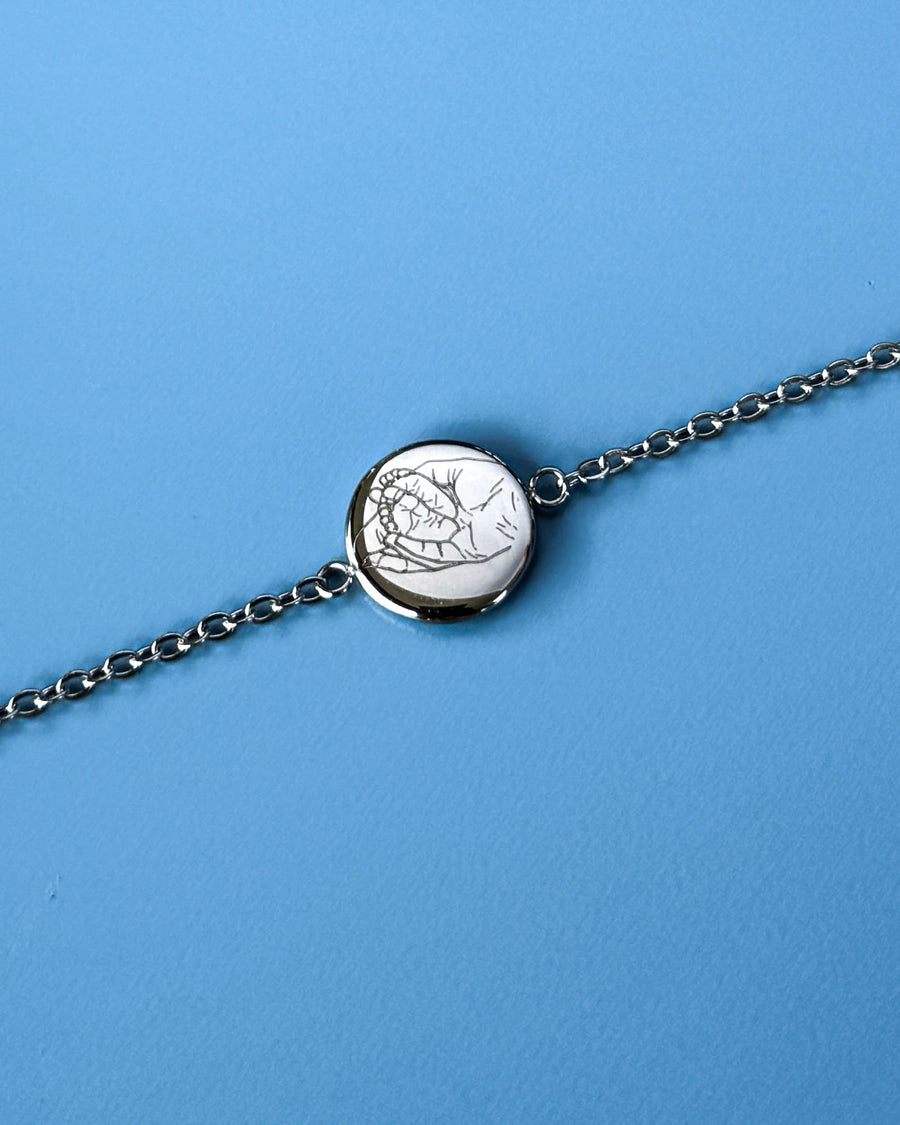IBI PORTRAIT bracelet in silver-coloured stainless steel with a line drawing of hands engraved on a round disc, against a blue background