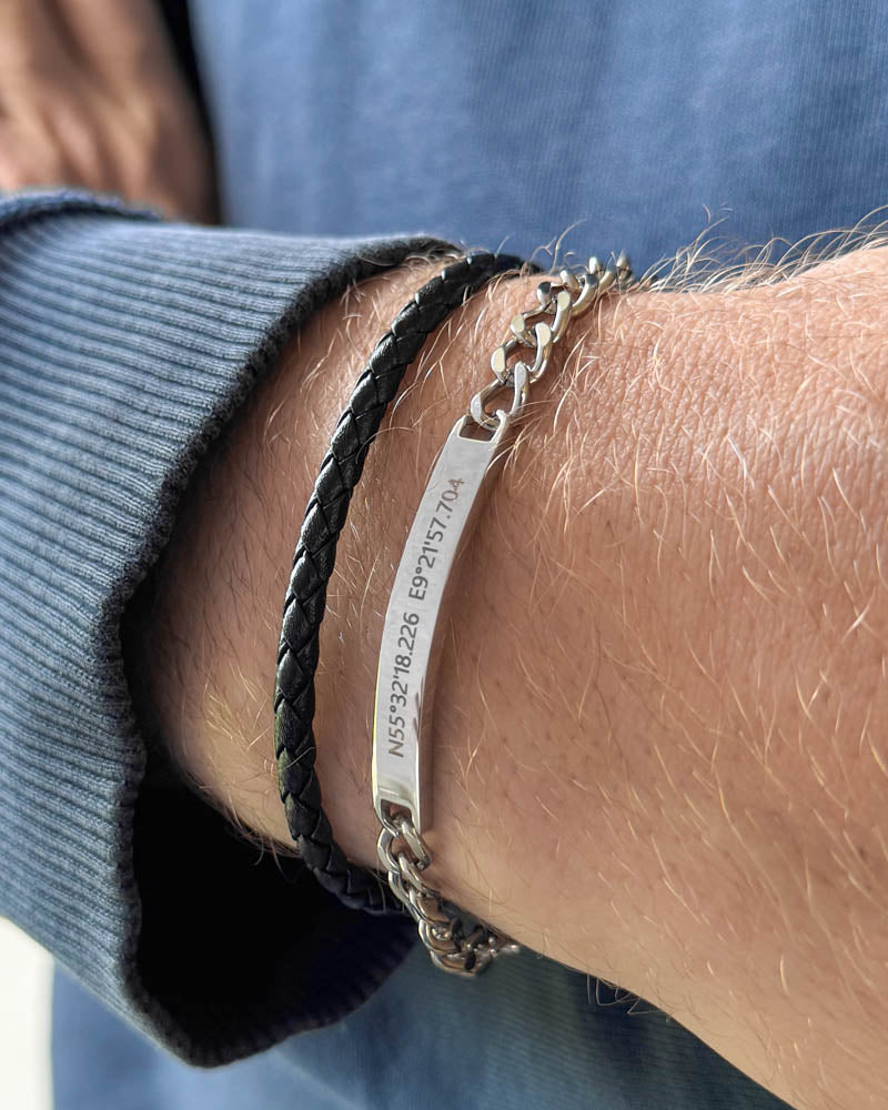 ARA bracelet in silver-coloured stainless steel, coordinates "N55°32'18.226 E9°21'57.704" engraved, with black braided leather bracelet