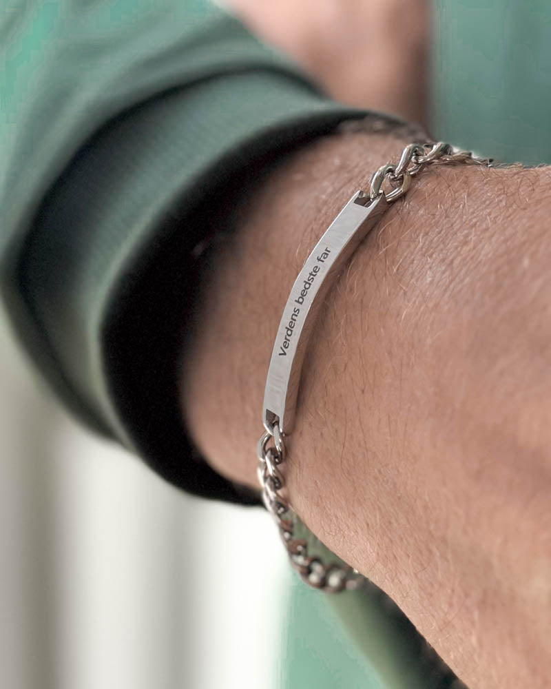 ARA bracelet in silver-coloured stainless steel with "Verdens bedste far" engraved on a bar plate, seen at an angle on the wrist