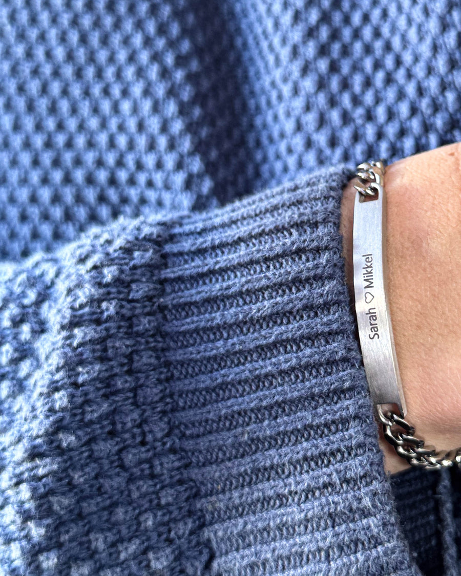 AVA bracelet in brushed silver-coloured stainless steel with "Sarah ♡ Mikkel" engraved, on the wrist with blue knit jumper