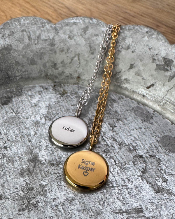 AYA QUOTE name necklaces in silver-coloured and gold-plated steel engraved with "Lukas" and "Signe Kasper" ♡, on a zinc tray