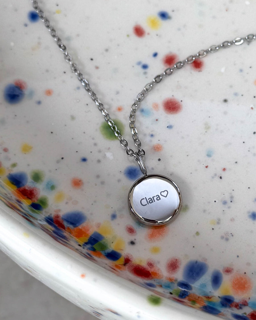 AYA NOTE name necklace in silver-coloured steel with the name "Clara" ♡ engraved on a small pendant, on a speckled ceramic dish