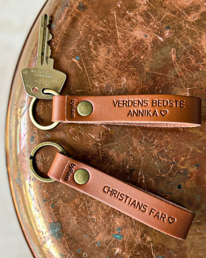 Two BOND leather keyrings in cognac with "Verdens bedste Annika" ♡ and "Christians far" ♡ engraved, on a copper tray with key