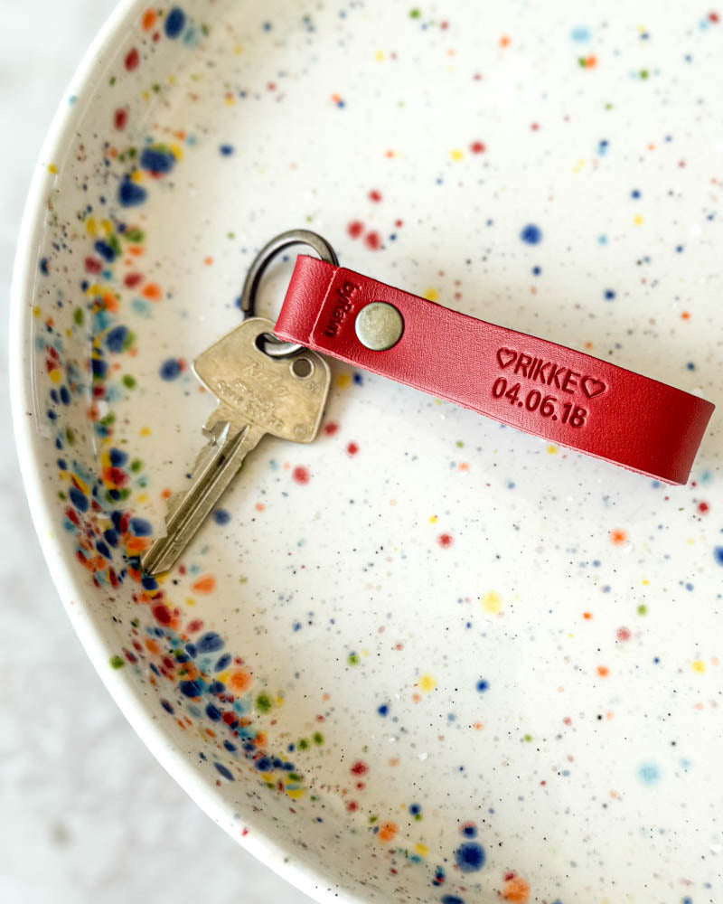 BOND leather keyring in red with the engraving "Rikke 04.06.18" ♡ and key in a white ceramic bowl with coloured dots