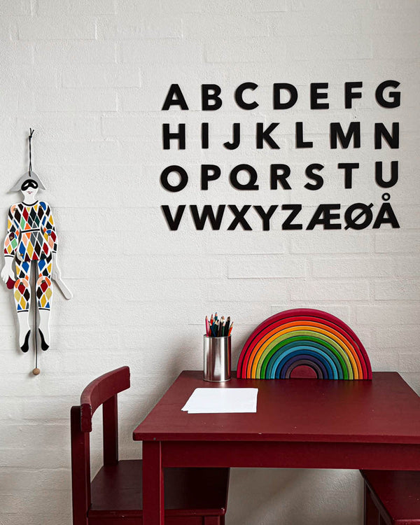 BOX leather letters in black as the full alphabet A–Å on a white brick wall above a red kids' table with wooden rainbow