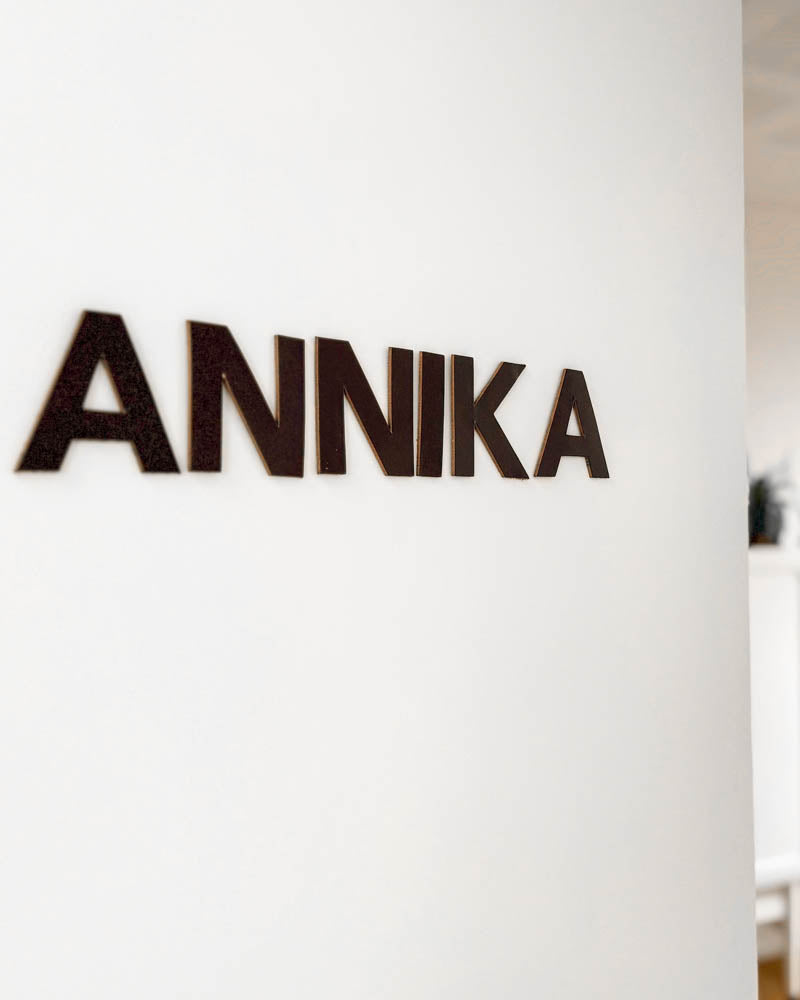 BOX leather letters in dark brown spelling the name "Annika" mounted on a white wall