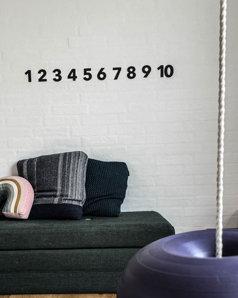 BOX leather numbers in black from 1 to 10 on a white brick wall above a dark green mattress with cushions and swing