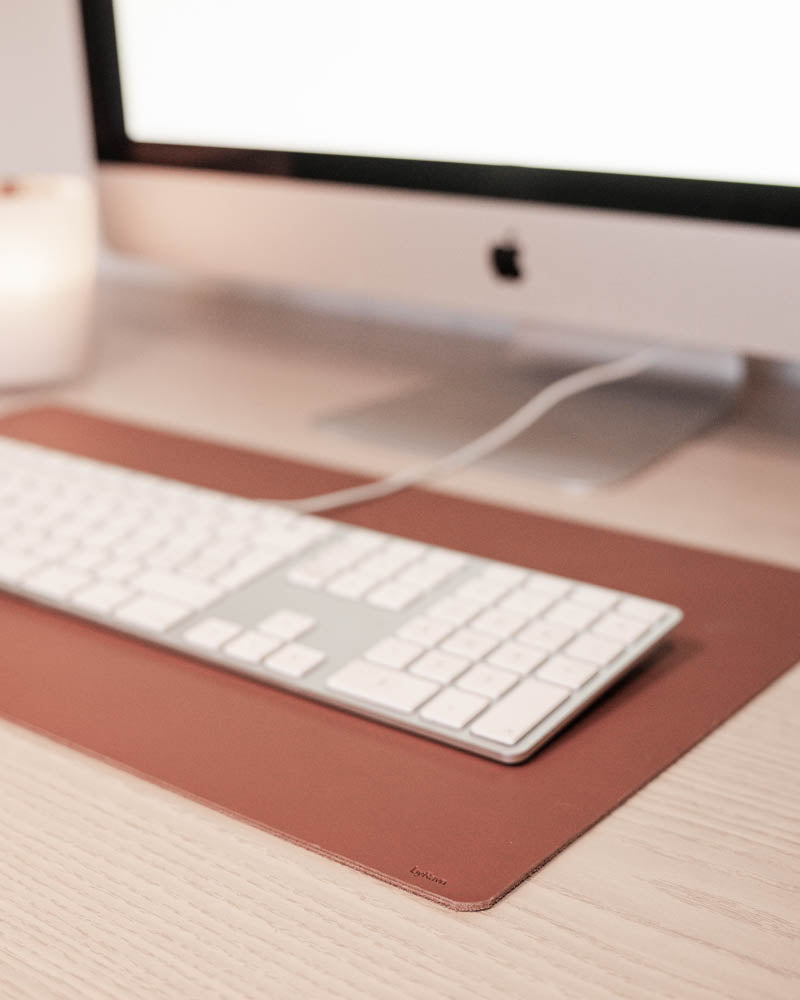 DESK desk pad in cognac leather under a white keyboard in front of an iMac on a light wooden desk