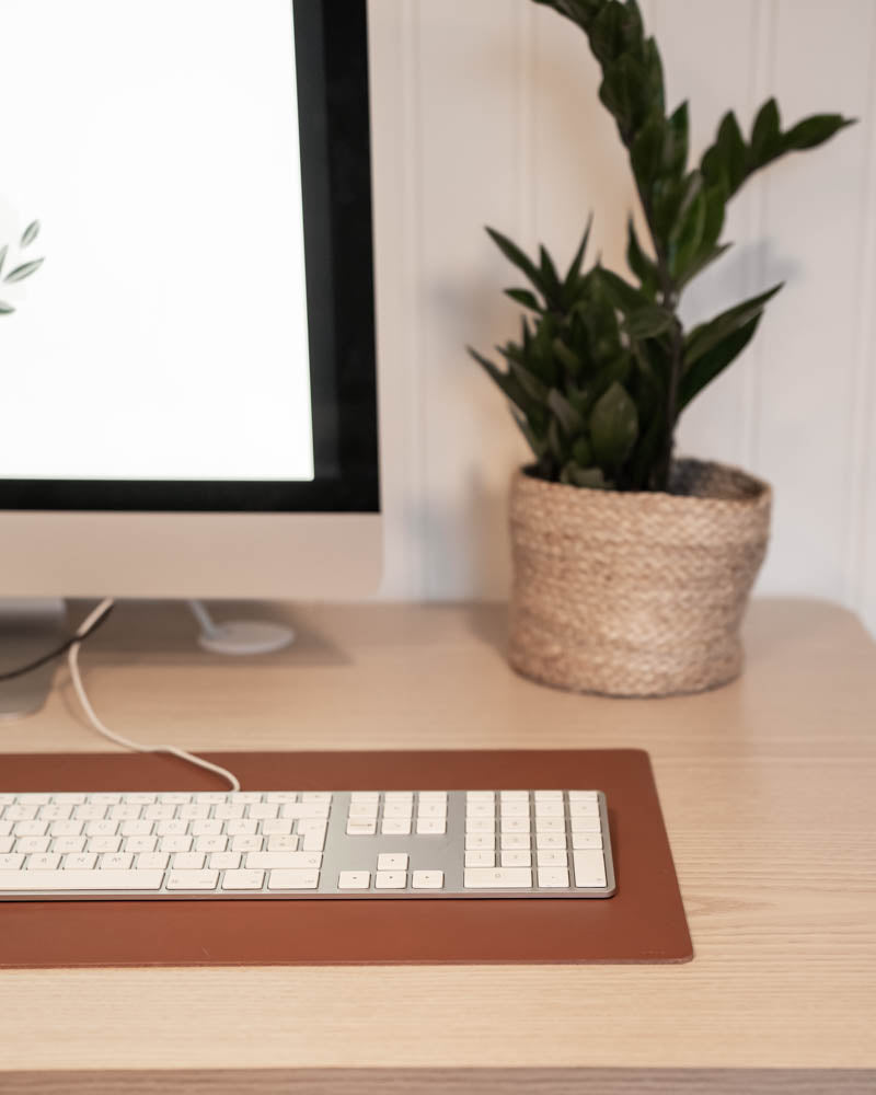 XXL DESK desk pad in cognac leather under a keyboard in front of an iMac with a green plant in a wicker basket