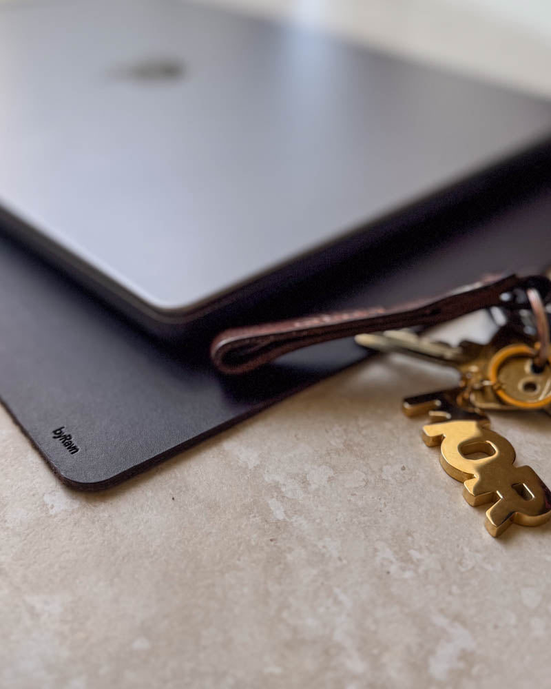 DESK desk pad in dark brown leather under a laptop with a leather keyring and gold-coloured key charm