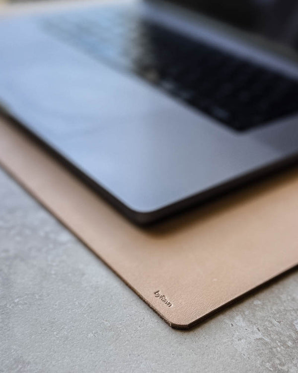 DESK desk pad in natural full-grain leather with byRavn embossing under a laptop on a light tabletop