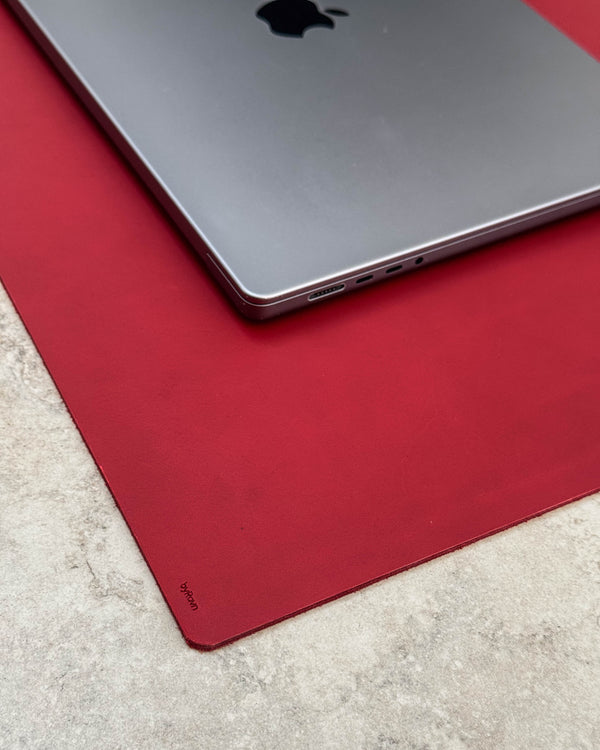 DESK desk pad in red full-grain leather with byRavn embossing under a silver laptop on a light tabletop