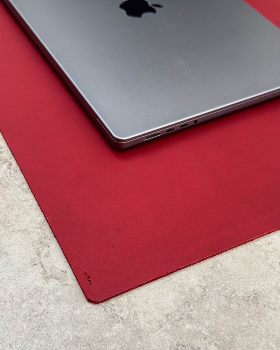 DESK desk pad in red full-grain leather with byRavn embossing under a silver laptop on a light tabletop