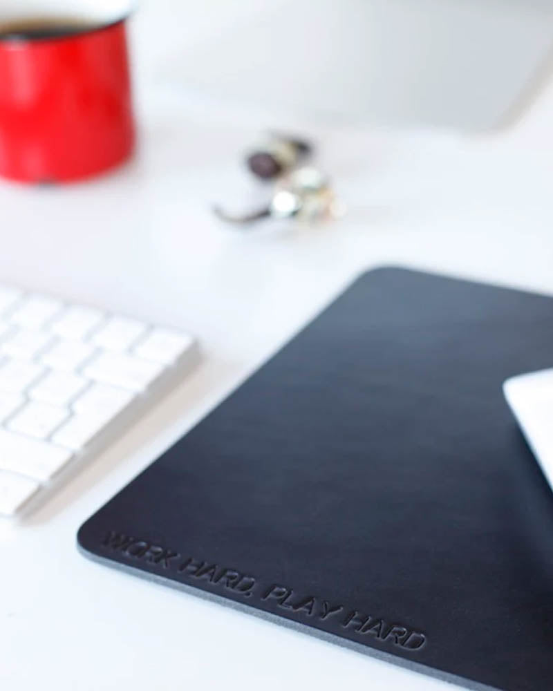 DOS mouse pad in black leather with the engraving "Work hard, play hard" on a desk with keyboard and red cup