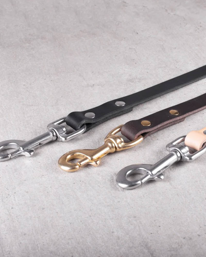 DOX160 leather dog leash in dark brown leather with brass carabiner, shown between black and natural leash with steel hooks on concrete